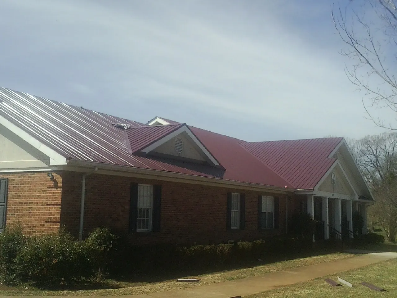 Red metal roof with gabled entries on a long brick building, from a Hail Damage Roof Repair job in Chicago