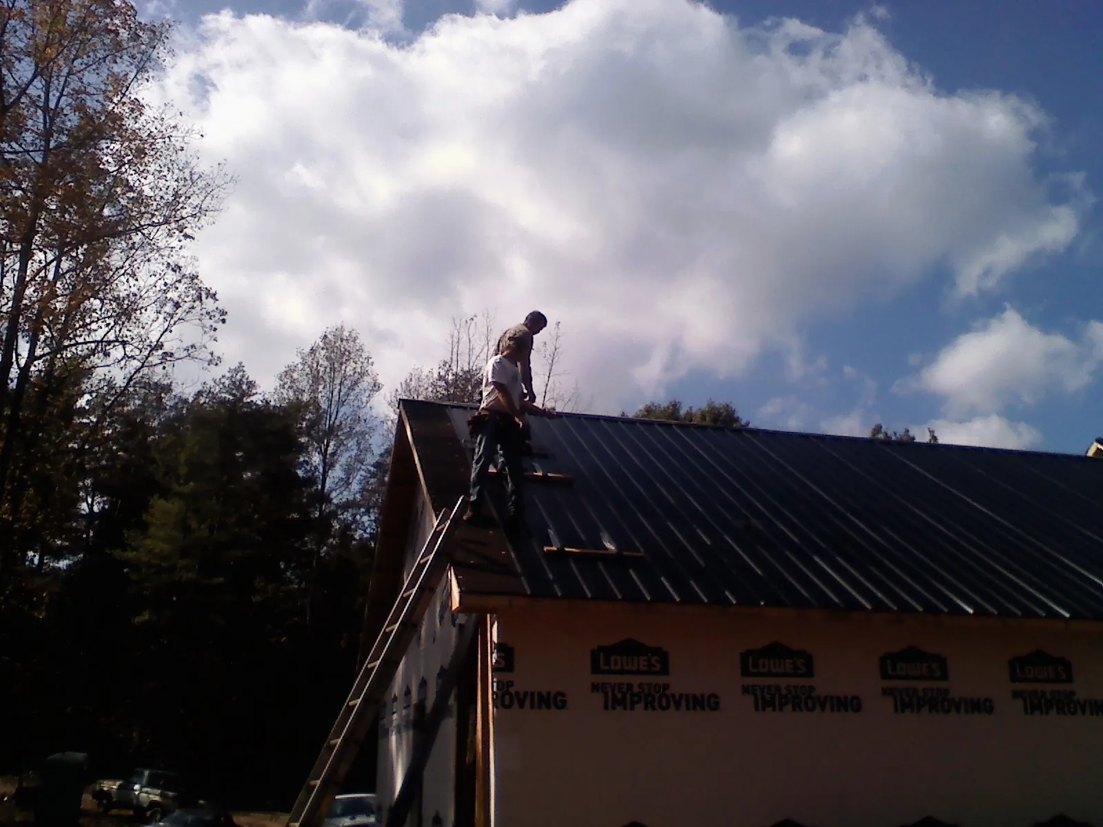 Roofer fastening dark metal panels high against a cloudy sky, from a Roof Inspection job in Chicago