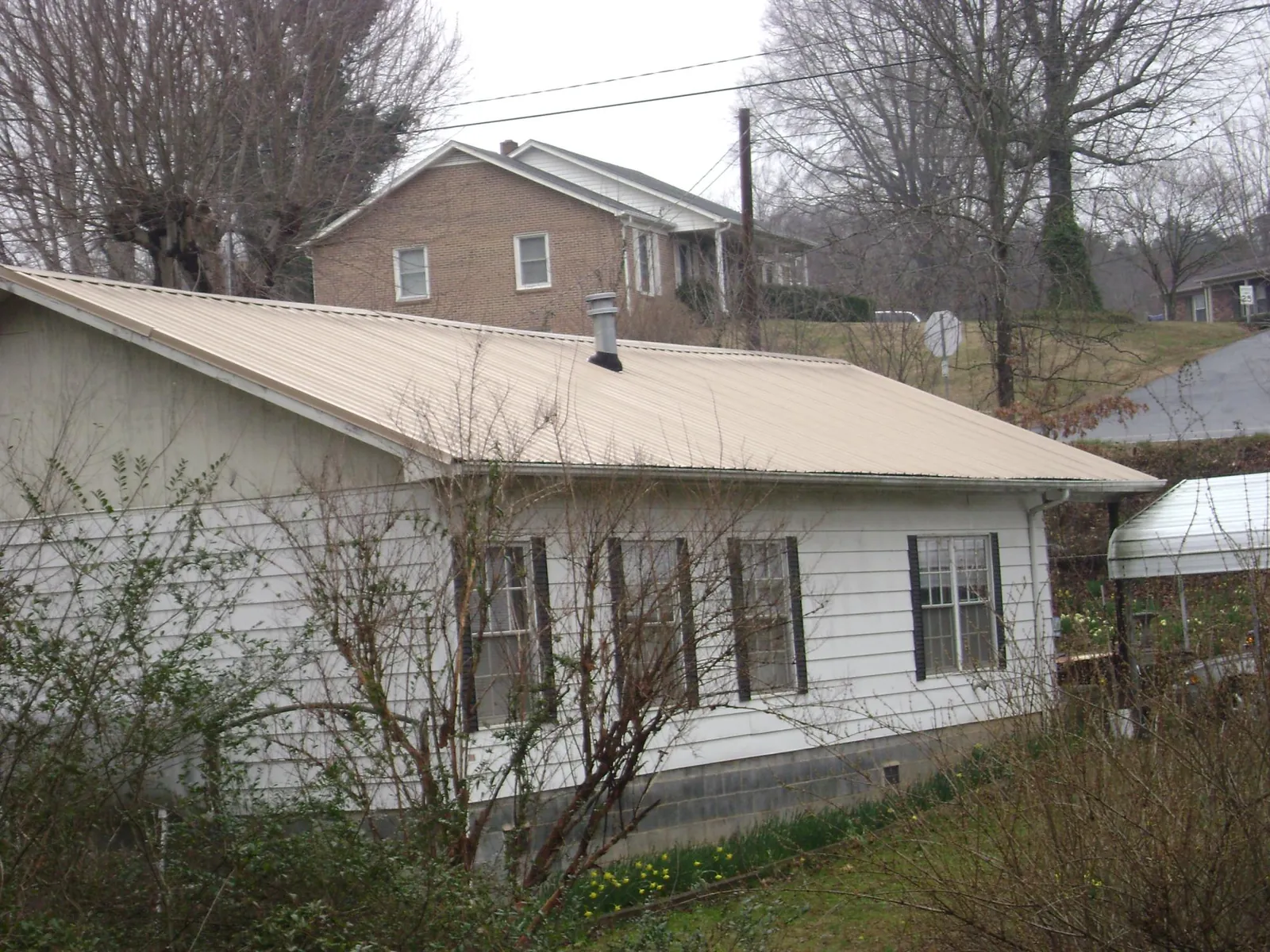 Tan metal roof on a white sided house set into a hillside — Commercial Roofing by Roofing Brothers in Chicago